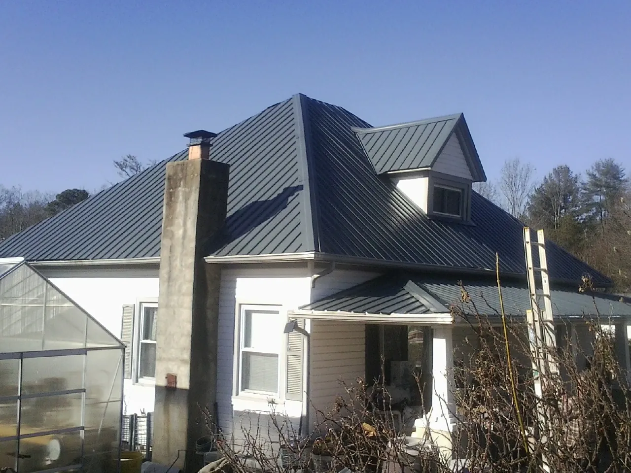 Dark blue standing seam metal roof on a white farmhouse with dormer — Slate & Tile Roof Repair by Roofing Brothers in Kaibeto