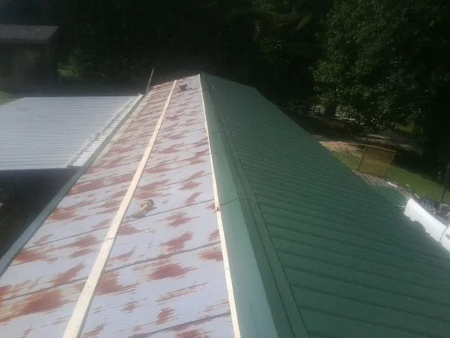 Old rusted panels beside newly installed green metal roofing — Wind Damage Roof Repair by Roofing Brothers in Kaibeto