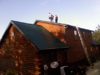 Crew on the ridge of a green metal roof on a two story log home in Kaibeto