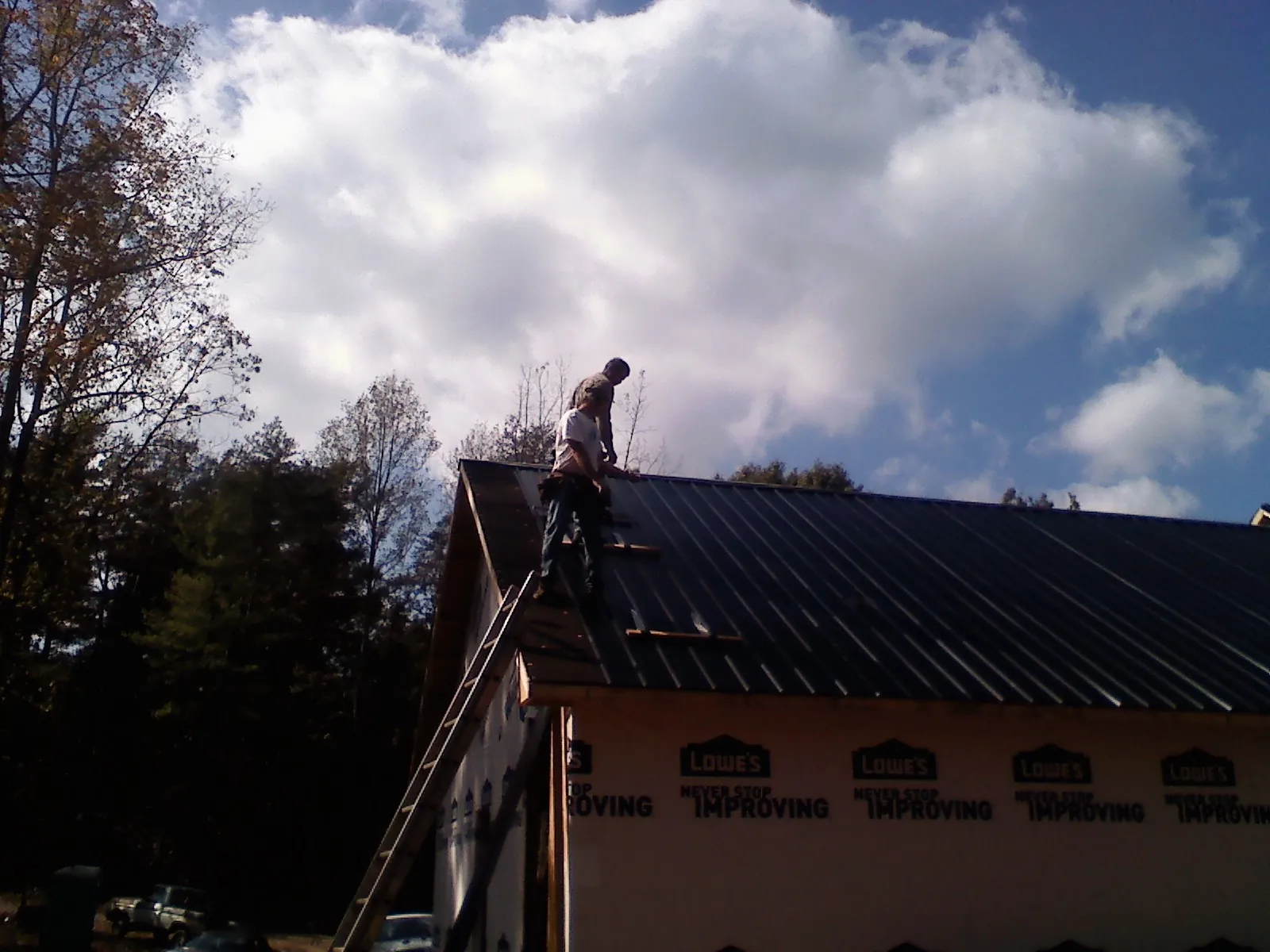 Roofer fastening dark metal panels high against a cloudy sky, from a Roof Inspection job in Kaibeto
