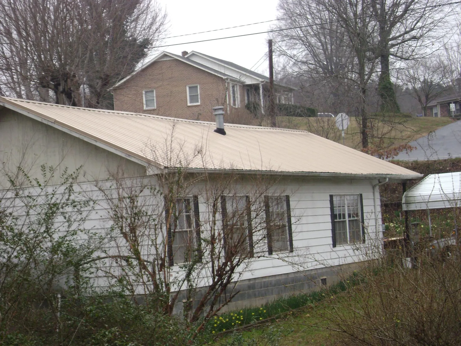 Tan metal roof on a white sided house set into a hillside — Commercial Roofing by Roofing Brothers in Kaibeto