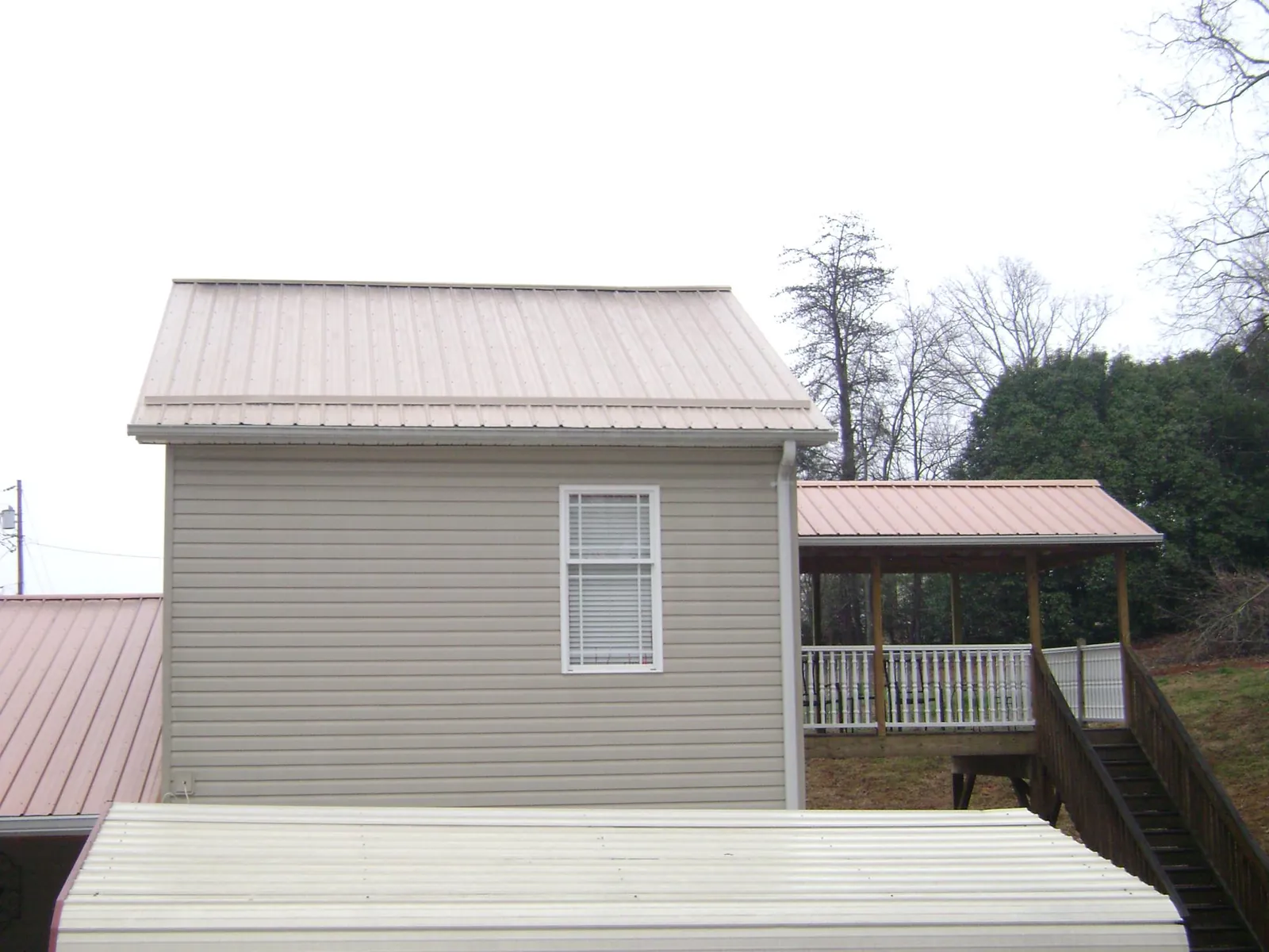 Tan metal roofs on a two story addition and attached porch, from a Roof Replacement job in Kaibeto